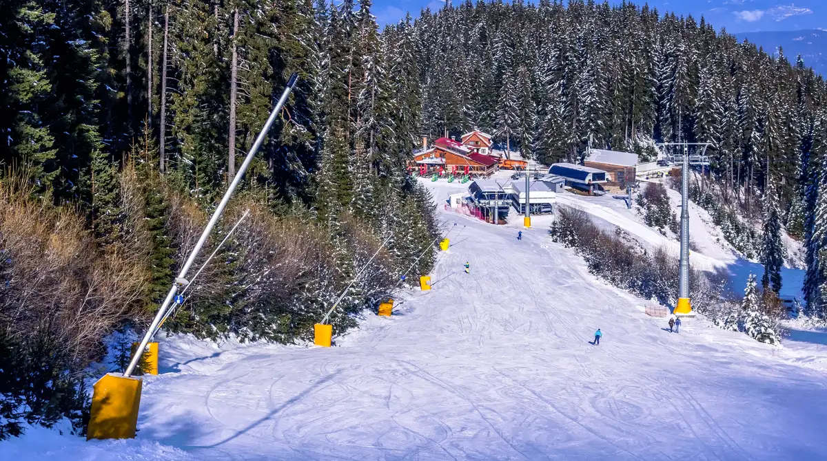 Skiatorë në një pistë të gjerë me diell mbi re në malet Pirin në Bansko, Bullgari