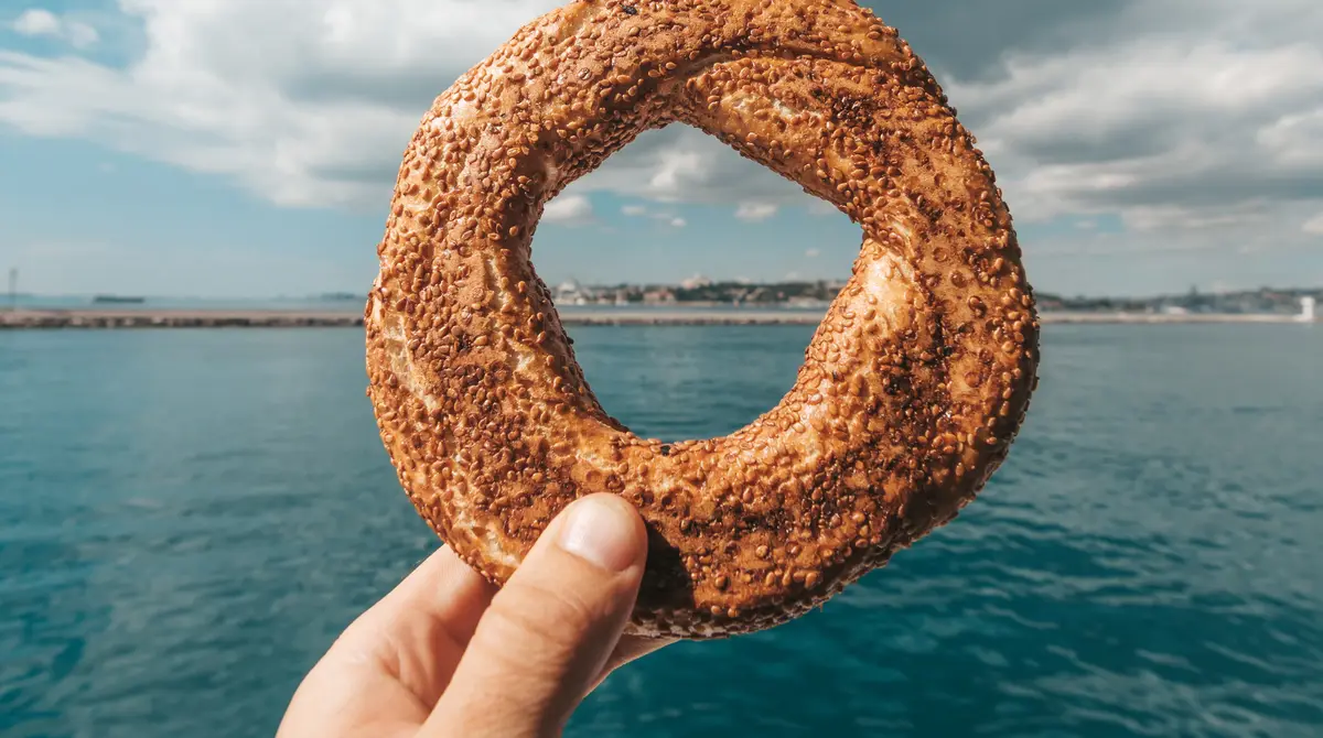 Dorë që mban një simit me susam me qytetin e vjetër të Stambollit dhe një xhami në sfond
