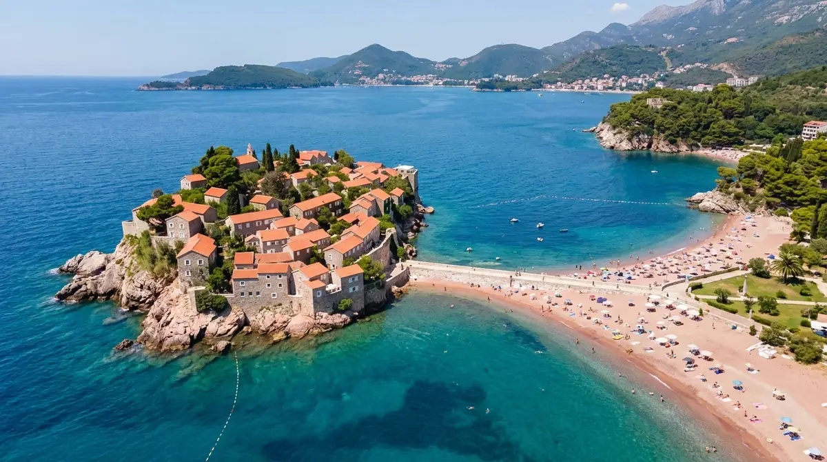 Pamje ajrore e ishullit Sveti Stefan në Mal të Zi me çati të kuqe, rërë lidhëse dhe ujë turkez të Adriatikut në verë