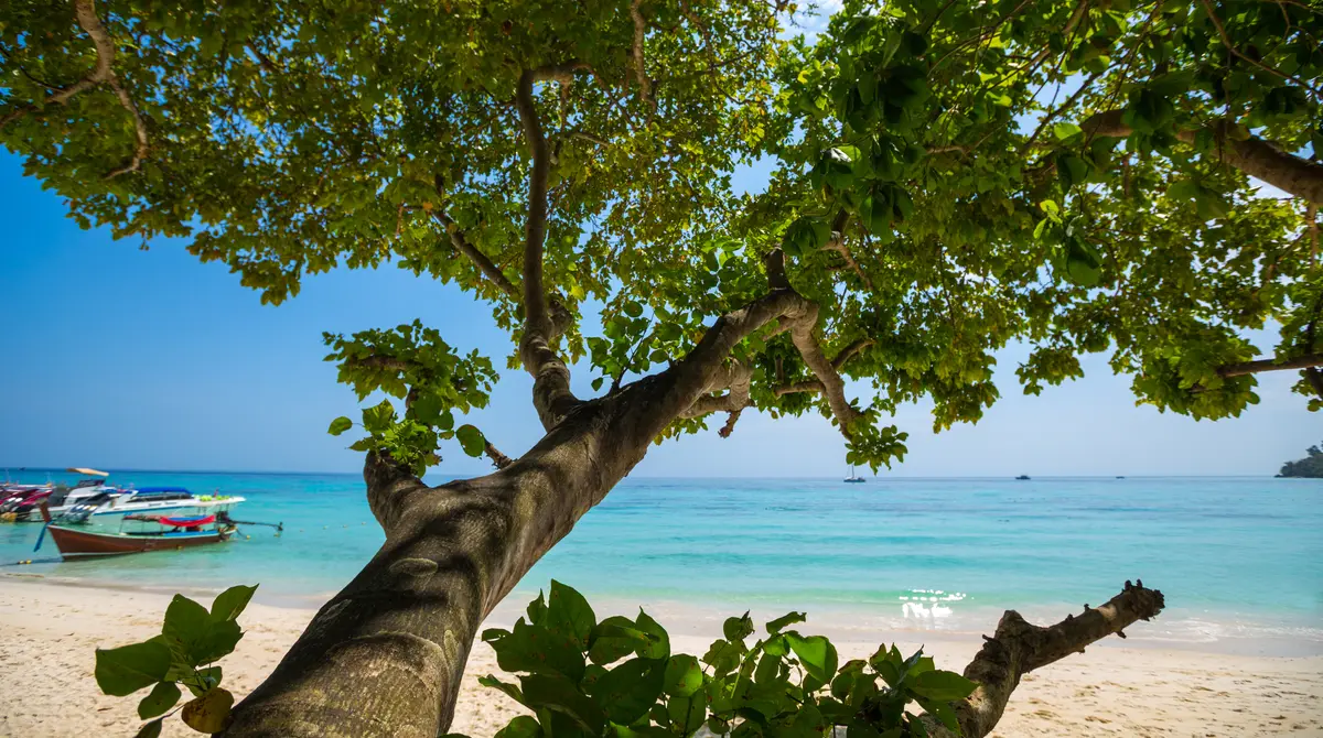 Tropical beach with clear turquoise water and longtail boats on the Andaman coast of Thailand