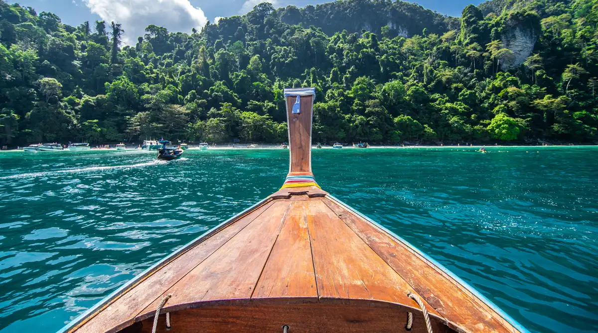 Traditional longtail boat approaching a jungle-backed beach in the Phi Phi islands, Thailand