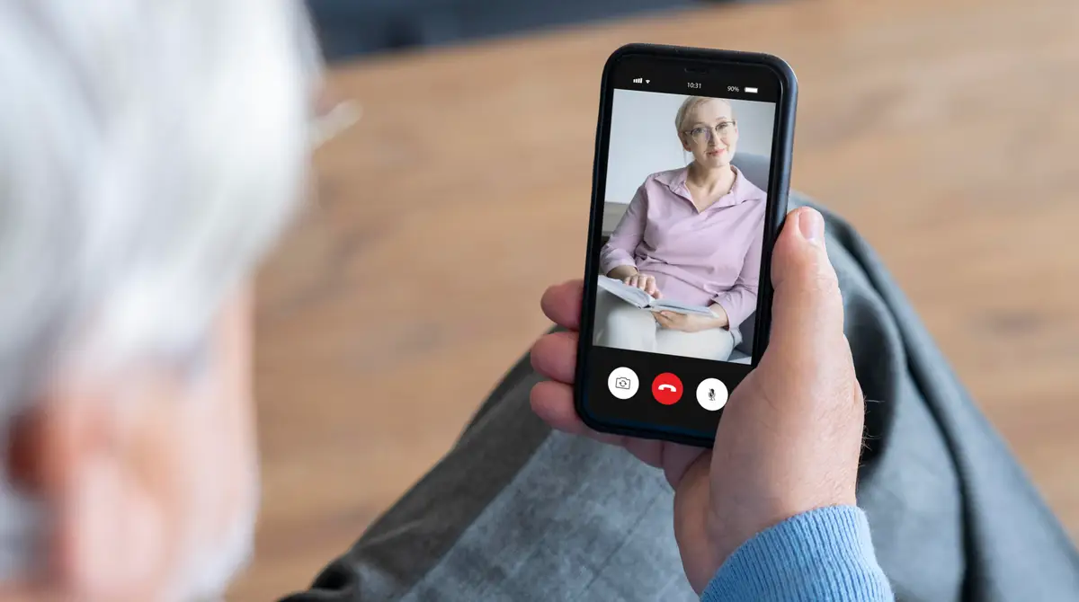 Burrë i moshuar që mban telefonin gjatë një videothirrjeje me një grua në ekran