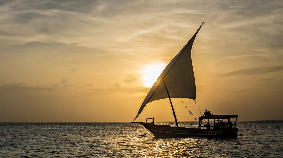 Traditional dhow sailing boat silhouetted against an orange sunset over the sea in Zanzibar