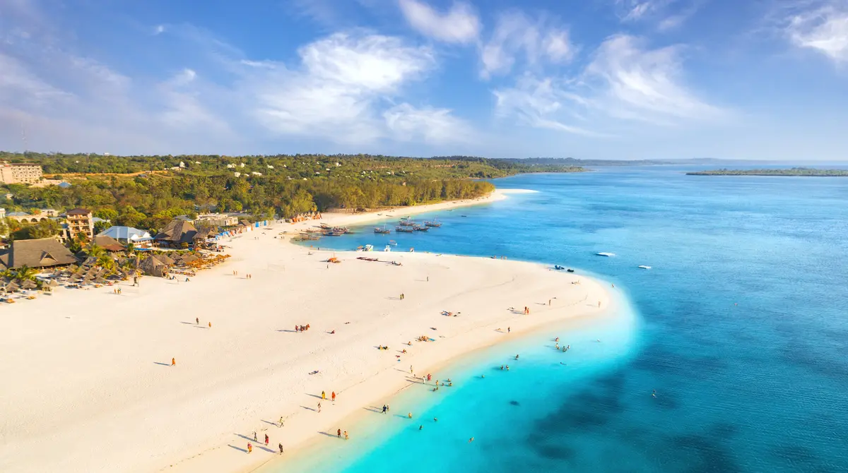 Aerial view of a white sand beach with palm trees and turquoise water in Zanzibar