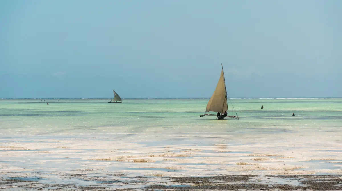 Traditional wooden dhow boat on turquoise water at a white sand beach in Zanzibar